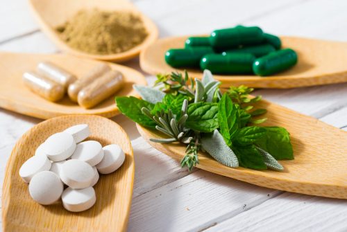 herbal leaves, ground herb powder and medicament pills on bamboo spoons, white wooden table