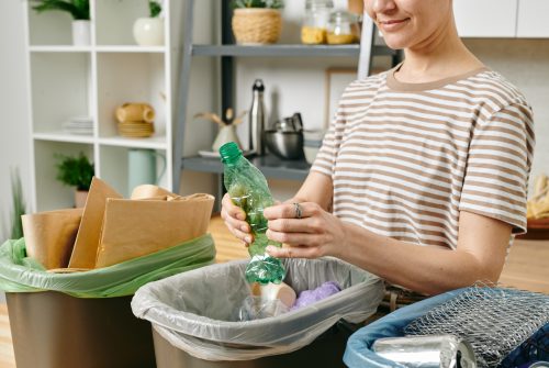 Young female smashing plastic bottle over one of three trash bins